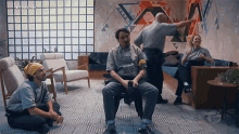 a group of people are sitting in a living room with a man sitting in a chair looking at his phone .