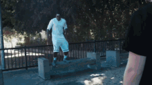 a man in a white shirt is jumping over a concrete bench