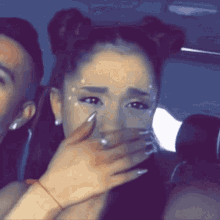 a woman is crying and covering her mouth with her hand while sitting in a car with a man .