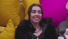 a woman is smiling while sitting on a couch surrounded by yellow and pink pillows .