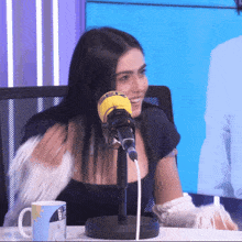 a woman is sitting in front of a microphone with a mug that says ' big ' on it