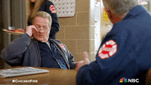 two men are sitting at a table with a chicago fire logo on their uniforms