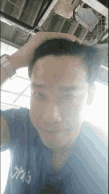 a man in a blue shirt is taking a selfie with his hand on his hair .