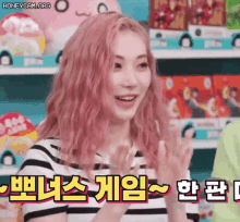 a woman with pink hair is clapping her hands in front of a shelf with toys .