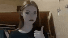 a woman is giving a thumbs up sign while standing in front of a piano .