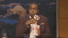 a man in a suit and bow tie is eating popcorn while wearing a face mask .