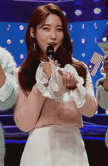 a woman is standing on a stage holding a microphone and a piece of paper .