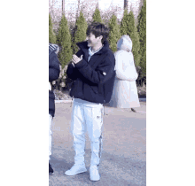 a man wearing a black jacket and white pants is standing in front of a statue .