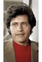 a close up of a man 's face with a brown jacket and a red turtleneck