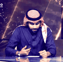 a man wearing a head scarf is sitting at a desk in front of a sign that says channels