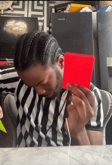 a man in a striped shirt is sitting at a table holding a red card .