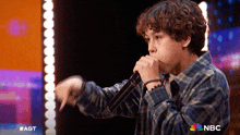 a young boy singing into a microphone with a nbc logo in the background