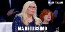 a woman with glasses is sitting in front of a crowd and says ma bellissimo