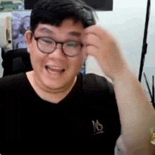 a man wearing glasses and a black shirt with the letter m on it is smiling