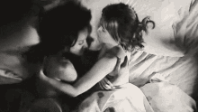 a black and white photo of two women hugging and kissing on a bed .