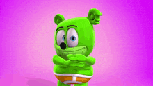 a green gummy bear is standing in front of a purple background