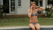a woman in a bikini is sitting on a ledge next to a pool .