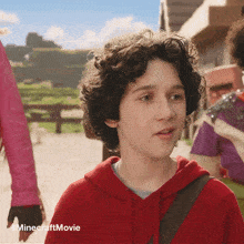 a young boy in a red hoodie stands in front of a minecraft movie poster