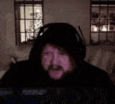 a man with a beard wearing headphones and a hooded jacket is laying in a bed .