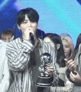 a man is holding a trophy and singing into a microphone while standing in front of a crowd .