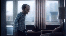 a man in pajamas is standing in a living room next to a couch and a lamp .