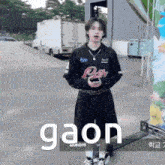 a young man is standing in a parking lot holding a cell phone and a sign that says gaon .
