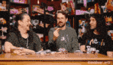 three men are sitting at a table with one wearing a shirt that says genesis