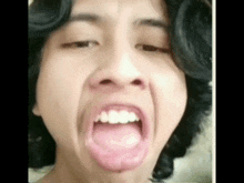 a young man with long hair is making a funny face with his mouth open .