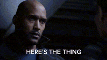 a bald man is sitting in a dark room with the words `` here 's the thing '' written on the screen .