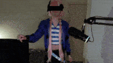 a person wearing a blue jacket and a pink wig stands in front of a microphone