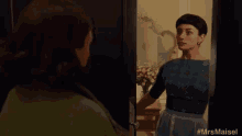 a woman in an apron is standing in front of a door looking at herself in the mirror .