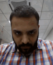 a man with a beard wearing a plaid shirt is looking at the camera
