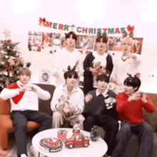 a group of young men are sitting around a table with christmas decorations in front of a christmas tree .