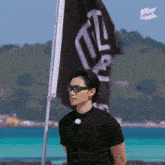 a man wearing sunglasses and a black shirt stands in front of a flag that says i think