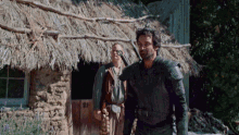 a man in armor stands in front of a thatched building with the number 81 on it