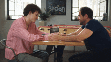 two men sit at a table with a sign that says spoon on it