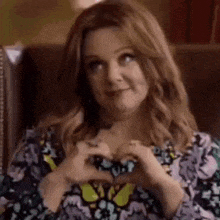 a woman is making a heart shape with her hands and smiling .