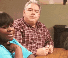 a man in a plaid shirt sits next to a woman in a blue shirt at a table