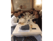 a group of people are sitting around a table holding a cake