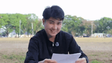 a young man in a black jacket is holding a piece of paper and smiling .