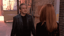 a man in a black jacket is talking to a woman