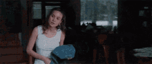a woman in a white tank top is sitting in front of a window and looking out .