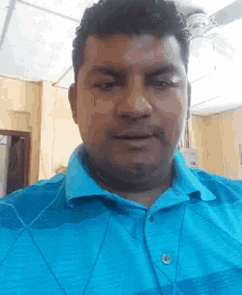 a man in a blue shirt with a ceiling fan in the background