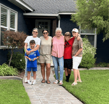 a group of people posing for a picture in front of a blue house with a boy in a red adidas shirt