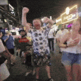 a man in a floral shirt is dancing in a crowded street at night