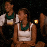a woman wearing a white tank top and a green scarf around her neck sits next to two other women .