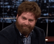 a man with a beard wearing a plaid shirt and a black jacket