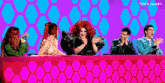 a group of people are sitting at a table applauding a drag queen 's performance .