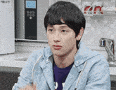 a young man wearing a blue jacket and a purple shirt is sitting in front of a microwave that says mochi on it