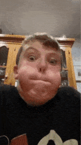 a young boy is making a funny face in front of a cabinet in a kitchen .